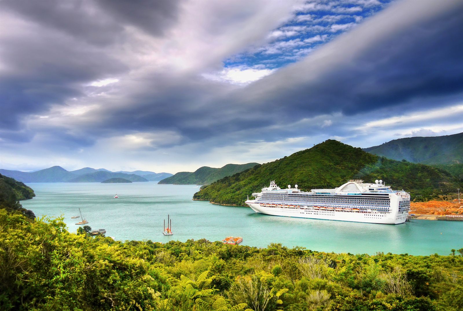 Cruise ship anchored in a green island bay under dramatic clouds